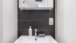 A bathroom with a white sink, dark tiled backsplash, a mirror above the sink, and a bottle of hand soap. - Cozy Antwerp Apartment Stay for 7 (Antwerp)