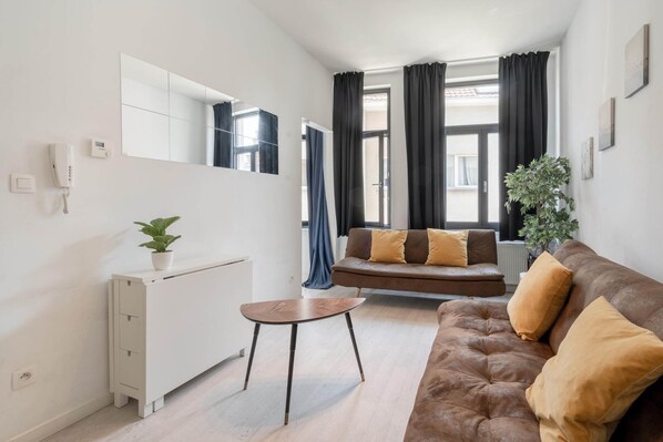 Una sala de estar moderna con un sofá, una mesita, un radiador, una planta en maceta y un gran ventanal con cortinas.