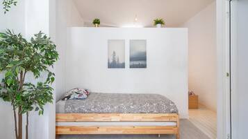 A bedroom with a wooden bed, two wall-mounted pictures, a potted plant, and a small wooden nightstand.