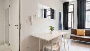 Una habitación moderna con un escritorio blanco, un sofá marrón, una planta en maceta y un espejo grande en la pared.