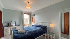 Quarto com cama, penteadeira, televisão, espelho e janela com cortinas.