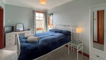 A bedroom with a bed, a dresser, a television, a mirror, and a window with curtains.