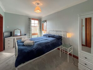 A bedroom with a bed, a dresser, a television, a mirror, and a window with curtains. - Avocet Apartment - UK51130 (Carradale)