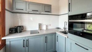 A modern kitchen with grey cabinets, a white countertop, a built-in oven, and a kettle.