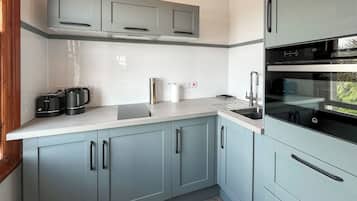 A modern kitchen with grey cabinets, a white countertop, a built-in oven, and a kettle.
