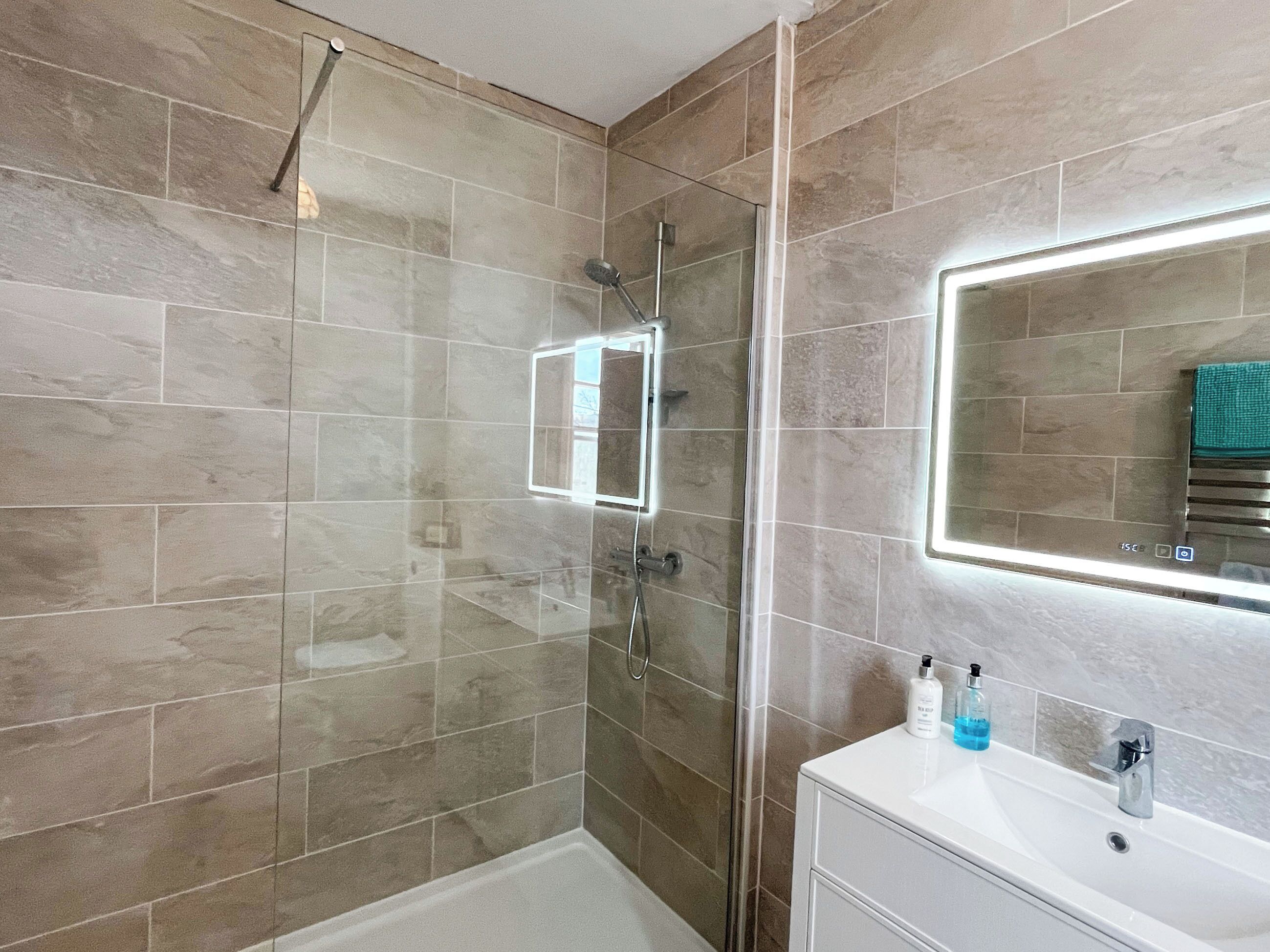 A modern bathroom with a glass-enclosed shower, a white vanity, and a mirror with integrated lighting.