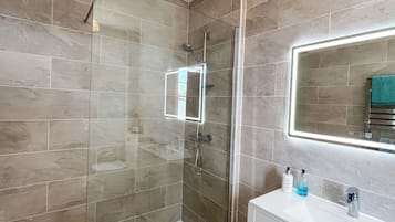 A modern bathroom with a glass-enclosed shower, a white vanity, and a mirror with integrated lighting.