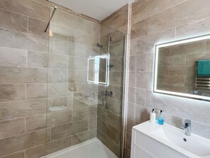 Une salle de bain moderne dotée d’une douche à parois de verre, d’un meuble-lavabo blanc et d’un miroir avec éclairage intégré.
