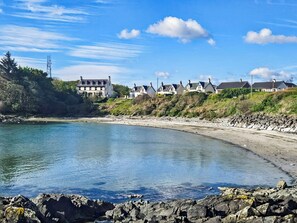 A coastal area with a rocky shoreline, a calm bay, and a row of houses with a prominent white building on the left.
