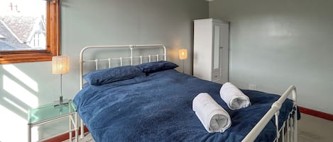 A bedroom with a bed, a nightstand, a lamp, a wardrobe, and a window with blinds.
