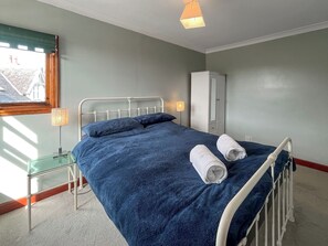 A bedroom with a bed, a nightstand, a lamp, a wardrobe, and a window with blinds.