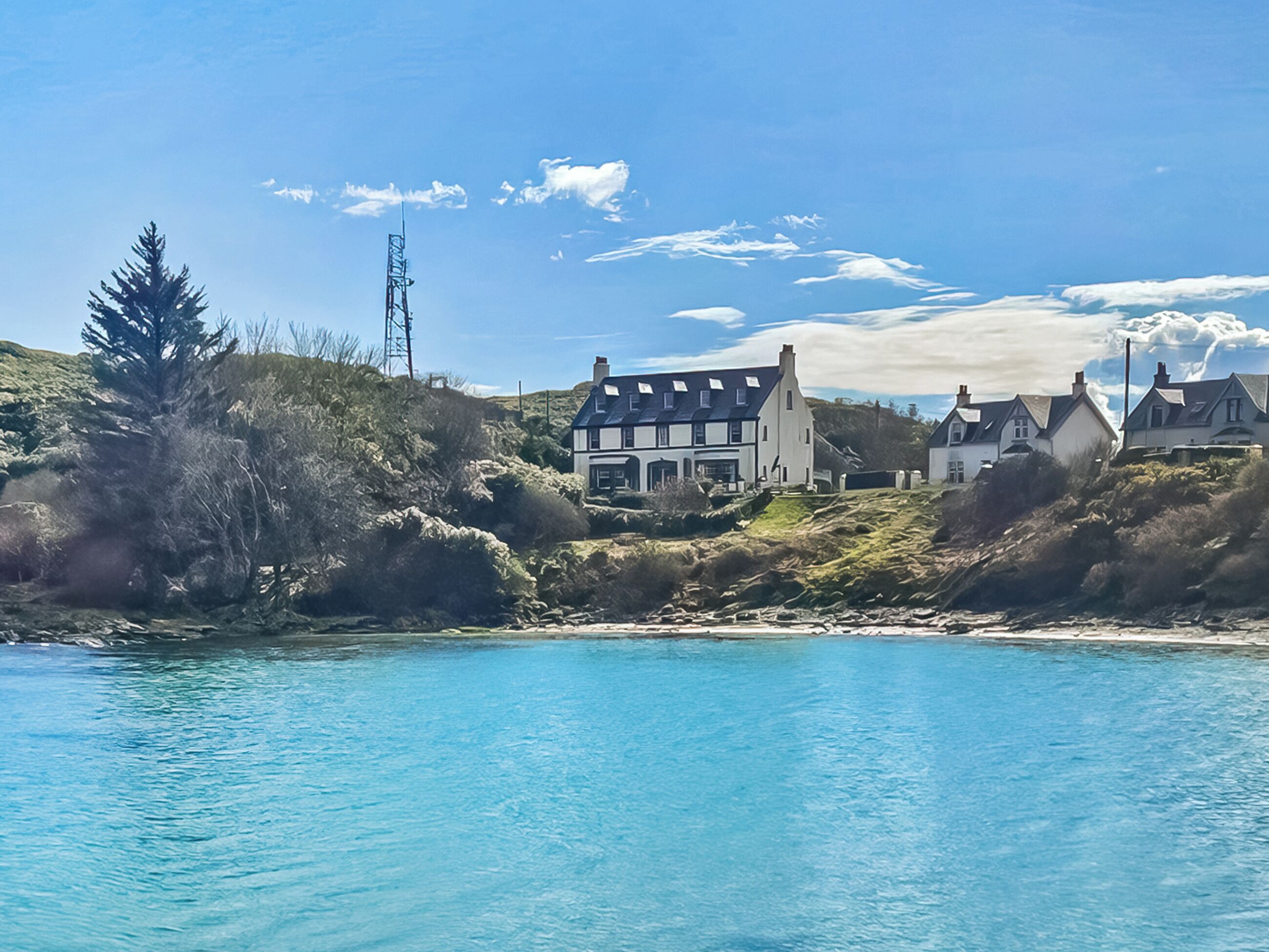A coastal property with a large house, a smaller building, and a hill with vegetation.