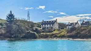 A coastal property with a large house, a smaller building, and a hill with vegetation.