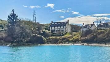 A coastal property with a large house, a smaller building, and a hill with vegetation.