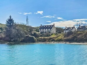 A coastal property with a large house, a smaller building, and a hill with vegetation.