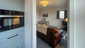 Cozinha com forno moderno, sala de jantar com mesa e cadeiras, e sala de estar com sofá e televisão.