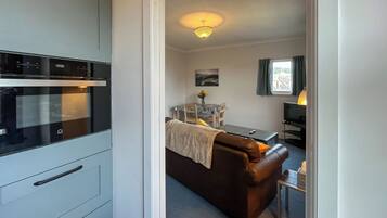 A kitchen with a modern oven, a dining area with a table and chairs, and a living area with a sofa and a TV.