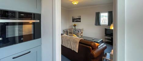 A kitchen with a modern oven, a dining area with a table and chairs, and a living area with a sofa and a TV.