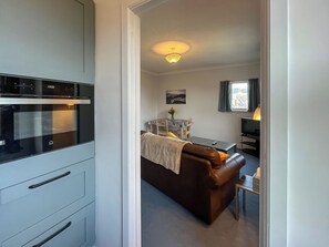 A kitchen with a modern oven, a dining area with a table and chairs, and a living area with a sofa and a TV. - Avocet Apartment - UK51130 (Carradale)
