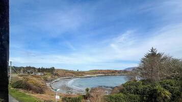 A coastal landscape with a curved beach, greenery, and a clear sky.