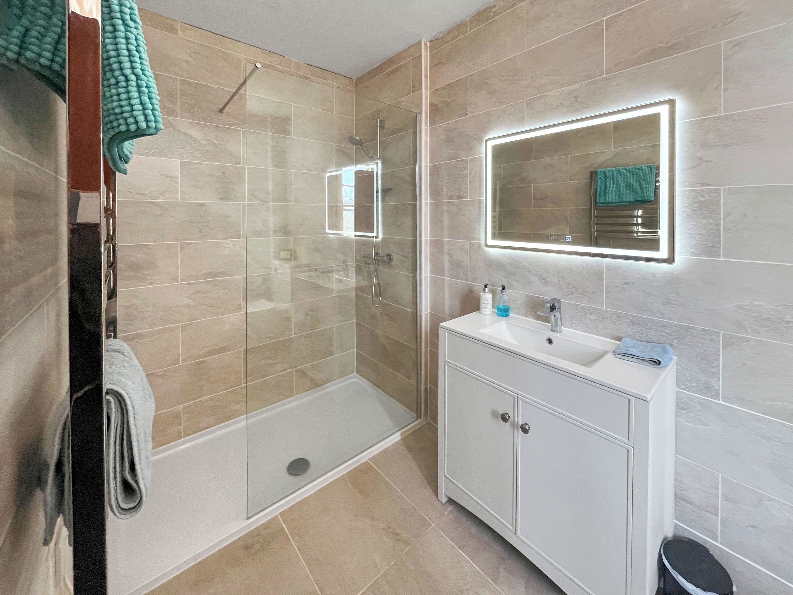 A modern bathroom with a glass-enclosed shower, a vanity with a mirror, and beige tiled walls.