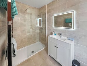 A modern bathroom with a glass-enclosed shower, a vanity with a mirror, and beige tiled walls. - Avocet Apartment - UK51130 (Carradale)