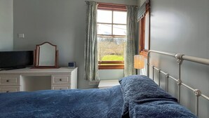 A bedroom with a bed, a dresser, a mirror, a window with curtains, and a radiator.