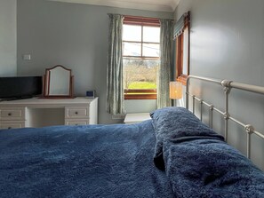 Une chambre à coucher comprenant un lit, une commode, un miroir, une fenêtre avec des rideaux et un radiateur.