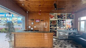 A wooden reception desk, a reception area, and a wall with food images and a sign saying 'People to eat are always the best people.' - Grand vista retreit  (Mussoorie)