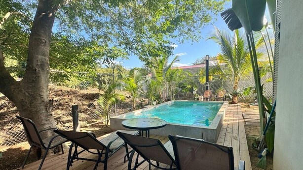A swimming pool with a wooden deck, surrounded by chairs and trees. - Comfortable 2BR Condo in Coco at Nangu (Coco)