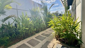 A pathway leading to a building with a fence and various plants. - Comfortable 2BR Condo in Coco at Nangu (Coco)