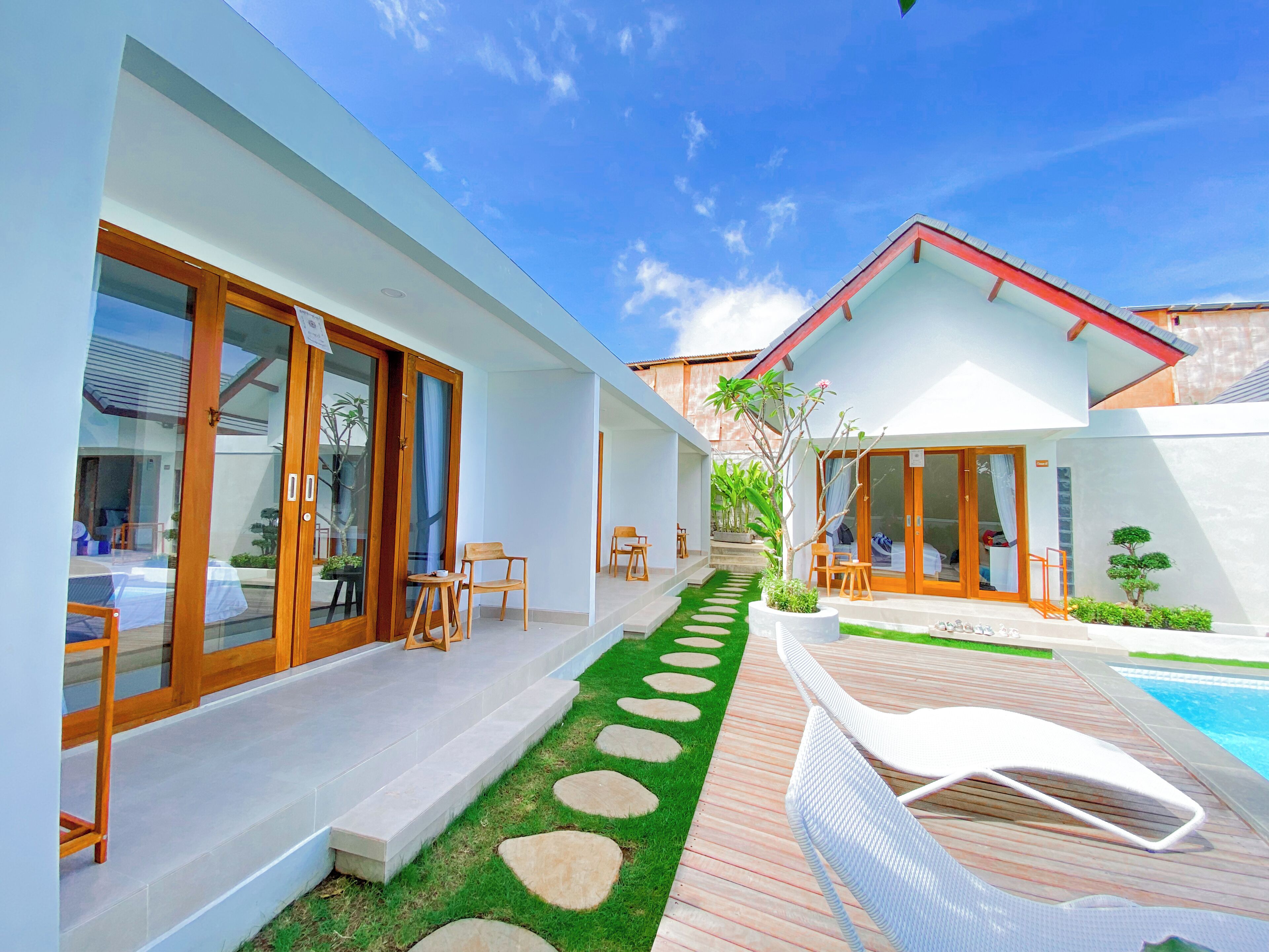 A modern house with a pool, a patio with lounge chairs, and a garden with stepping stones.