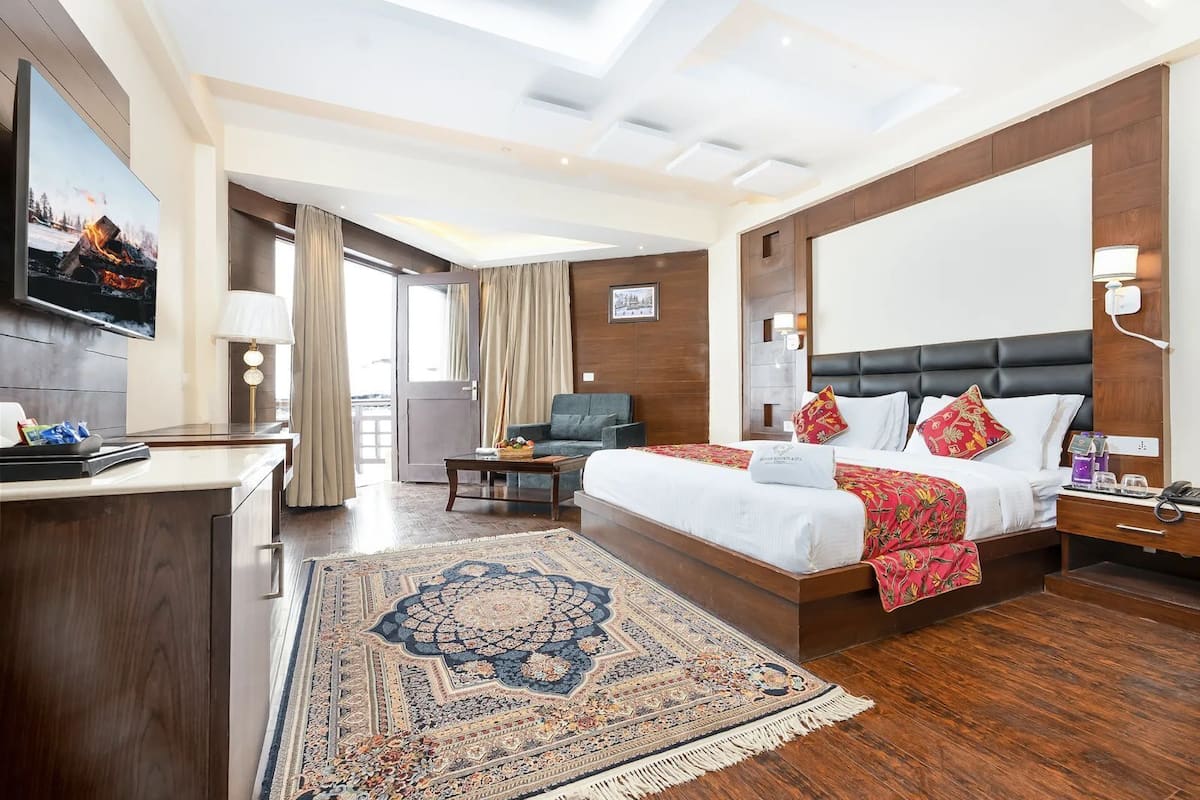 A hotel room with a large bed, a desk with a lamp, a TV, and a view of the outdoors.