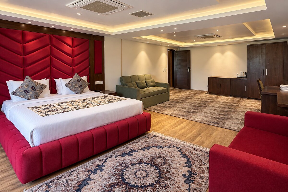 Un dormitorio moderno con una cama grande, un sofá verde, piso de madera y una pared de acento roja.