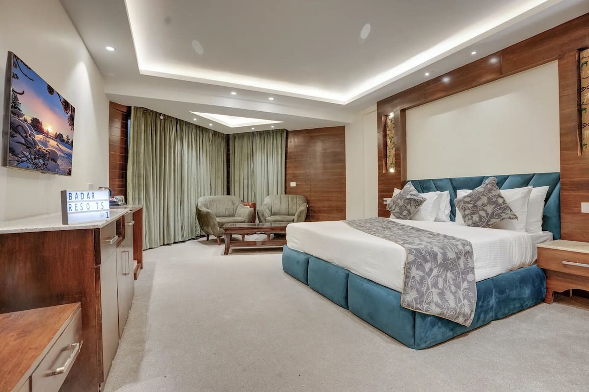 A modern bedroom with a large bed, a desk, a chair, and a view of the outdoors.