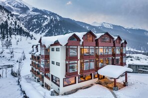 Un hotel de varios pisos con techo nevado, amplias ventanas y vistas a montañas cubiertas de nieve.