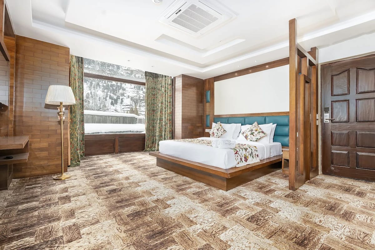 A bedroom with a bed, a desk, a lamp, and a view of a snowy landscape.
