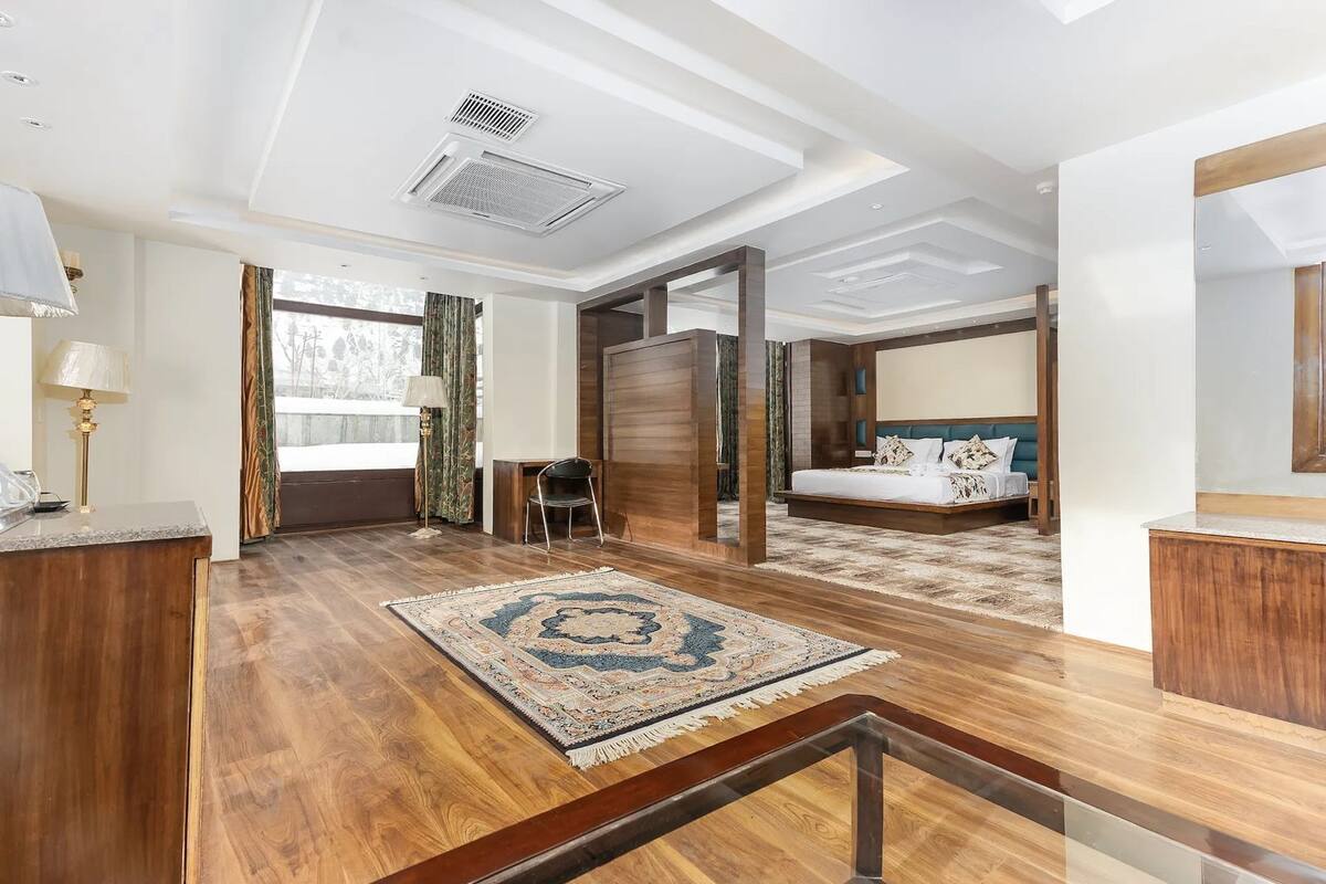 A spacious hotel room with a large bed, a sitting area with a chair, a desk, and a view of the outdoors.