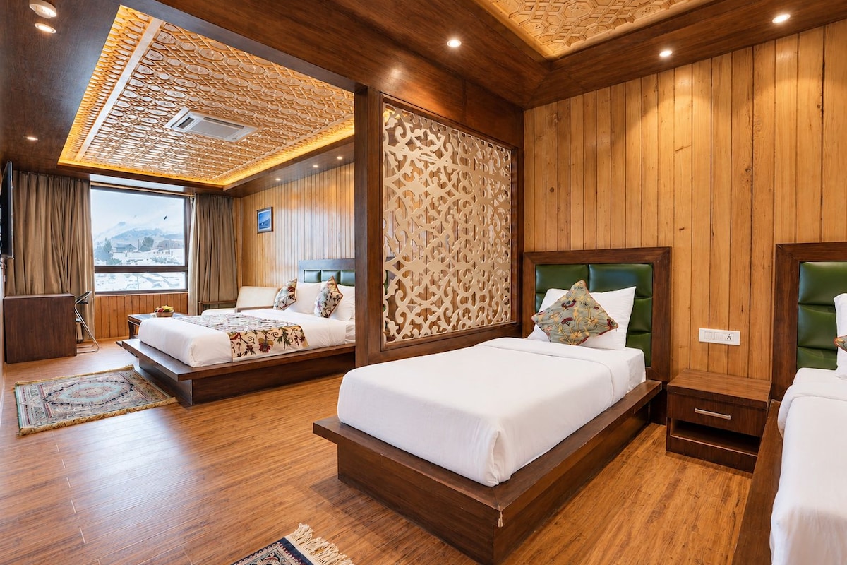 Habitación de hotel con dos camas, paneles de madera, techo decorativo y vista a un paisaje nevado.