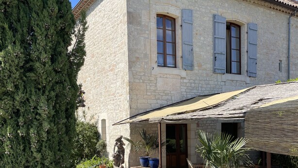 A stone building with a tiled roof, a covered patio, and a statue. - La Maison Soleil du Levant (Sérignac)