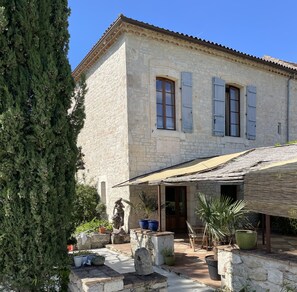 A stone building with a tiled roof, a covered patio, and a statue. - La Maison Soleil du Levant (Sérignac)