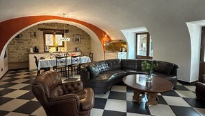 A spacious living area with a checkered floor, a leather sofa, a coffee table, and a dining area with a table and chairs. - La Maison Soleil du Levant (Sérignac)