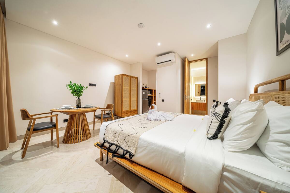 A modern hotel room with a bed, a desk, a chair, a potted plant, and a wardrobe.