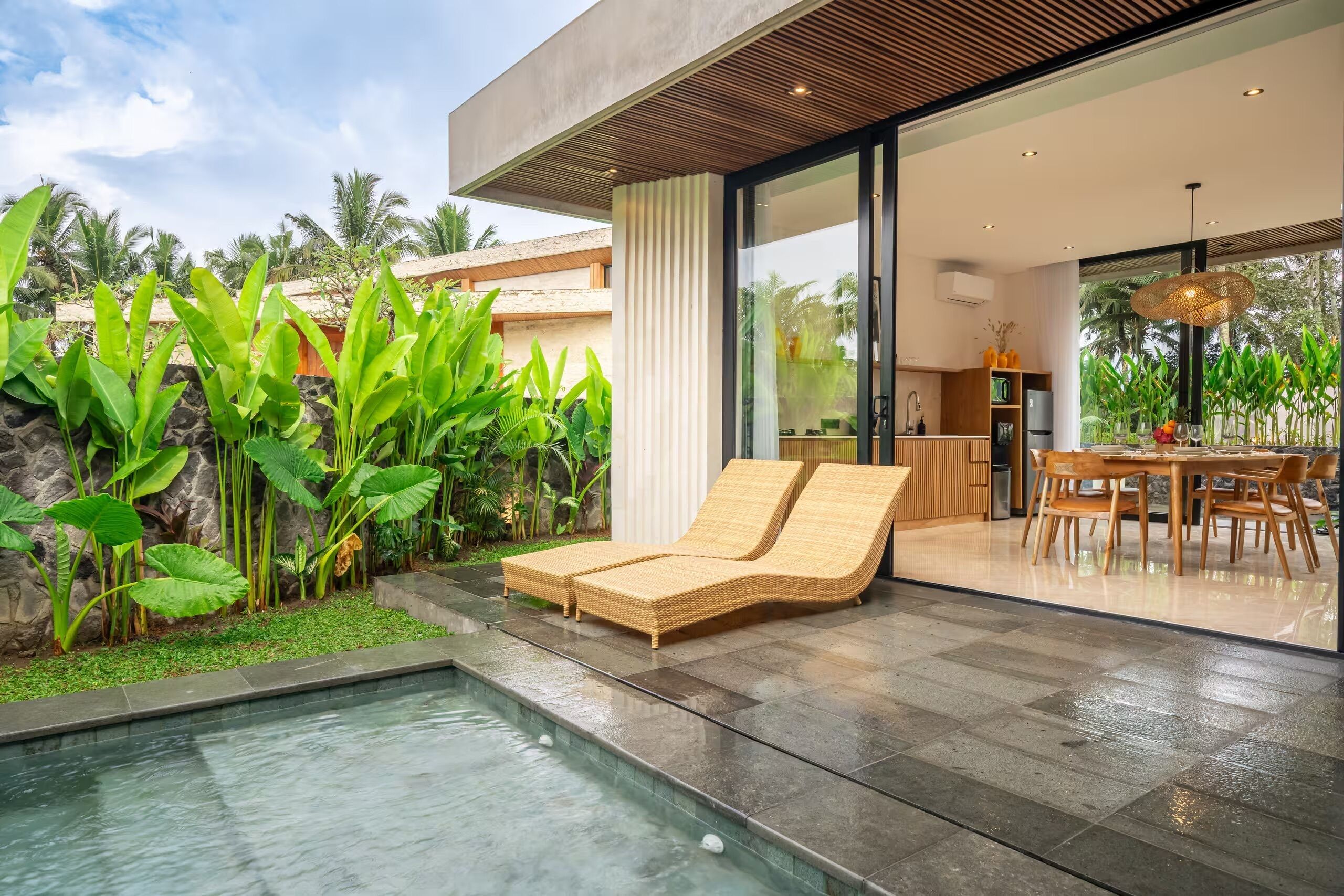 A modern house with a swimming pool, a dining area, and lush greenery.
