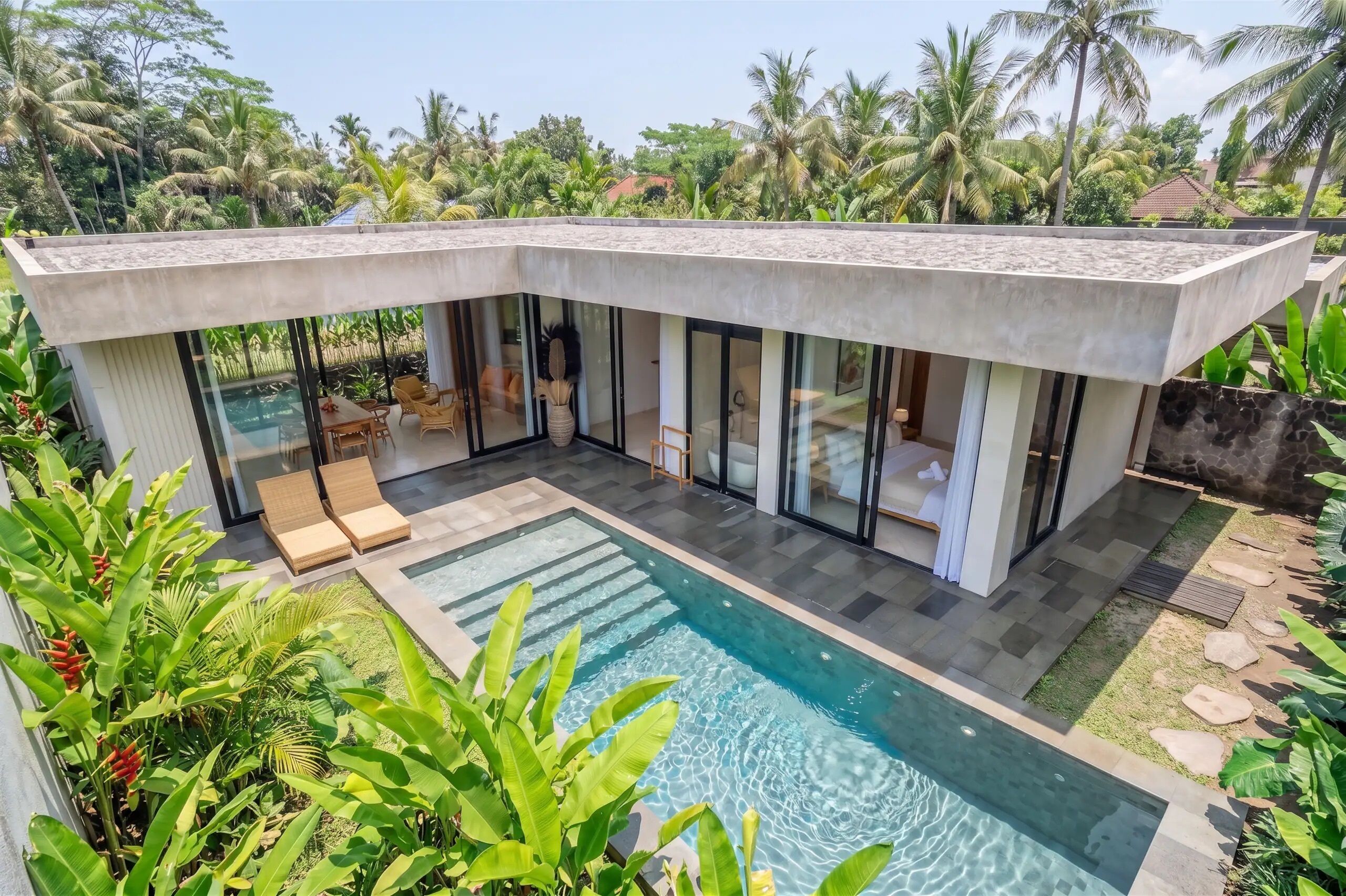 Una casa moderna con piscina, amplios ventanales y exuberante vegetación tropical.