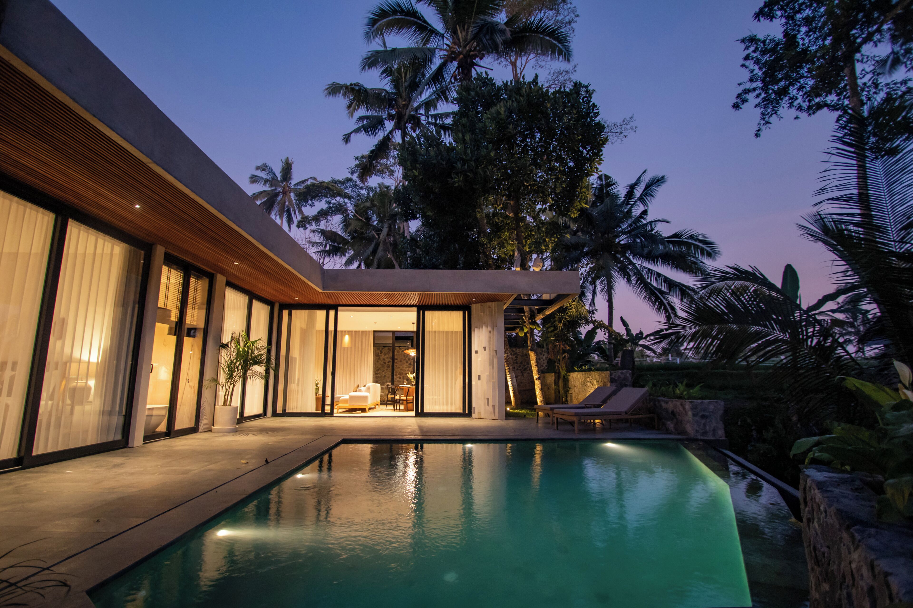 Una casa moderna con piscina, ventanas amplias y vistas a palmeras.