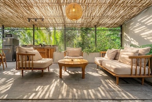 An outdoor seating area with a round wooden table, two sofas, and a kitchen area with a refrigerator. - Happiness Residence Ubud (Ubud)