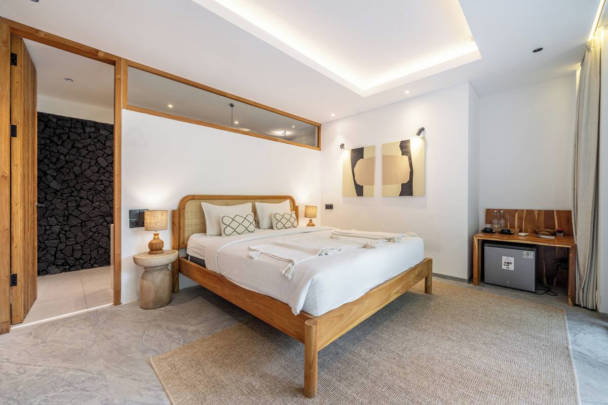 A modern bedroom with a wooden bed, a stone wall, a small desk, and a mirror.
