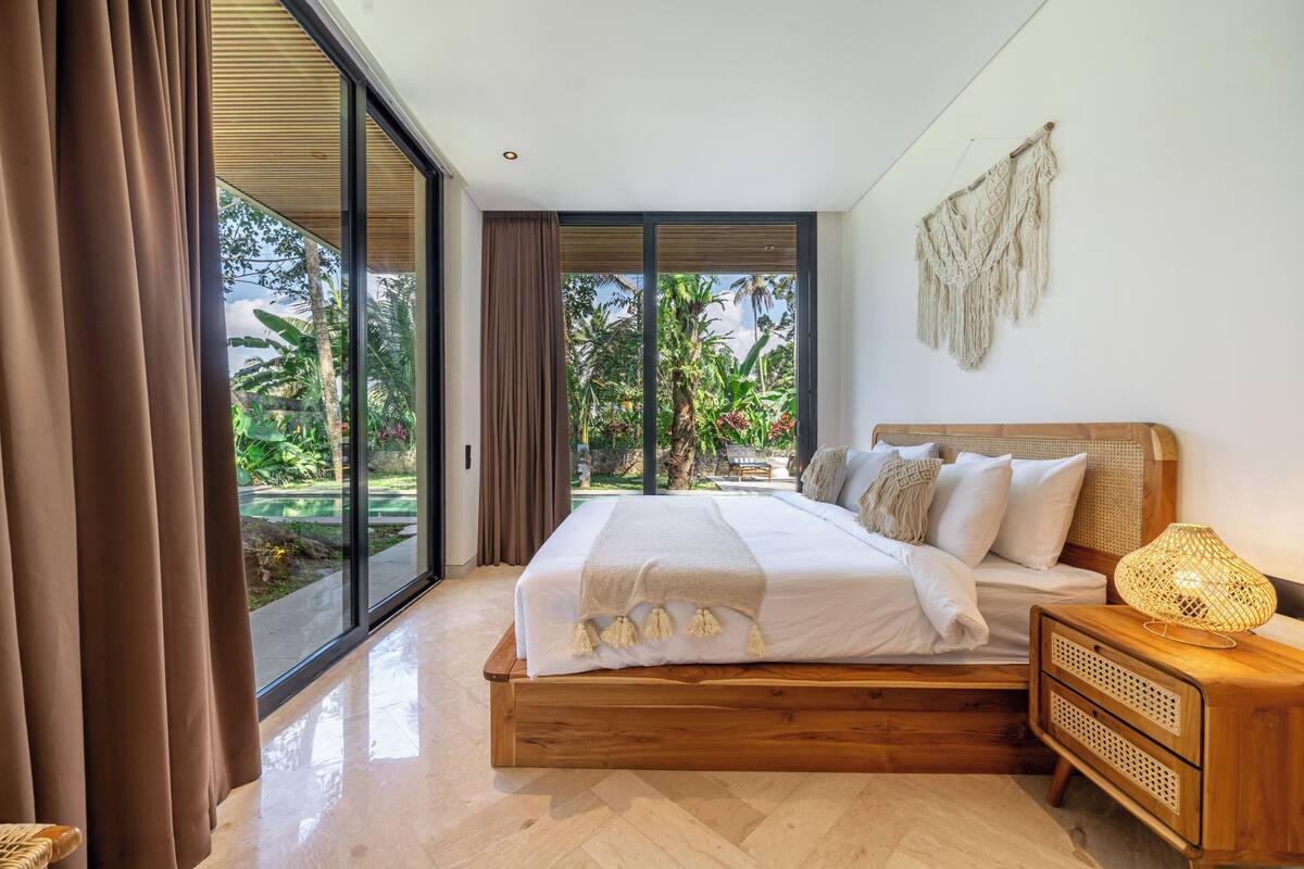 A bedroom with a large bed, wooden headboard, and a nightstand with a lamp.
