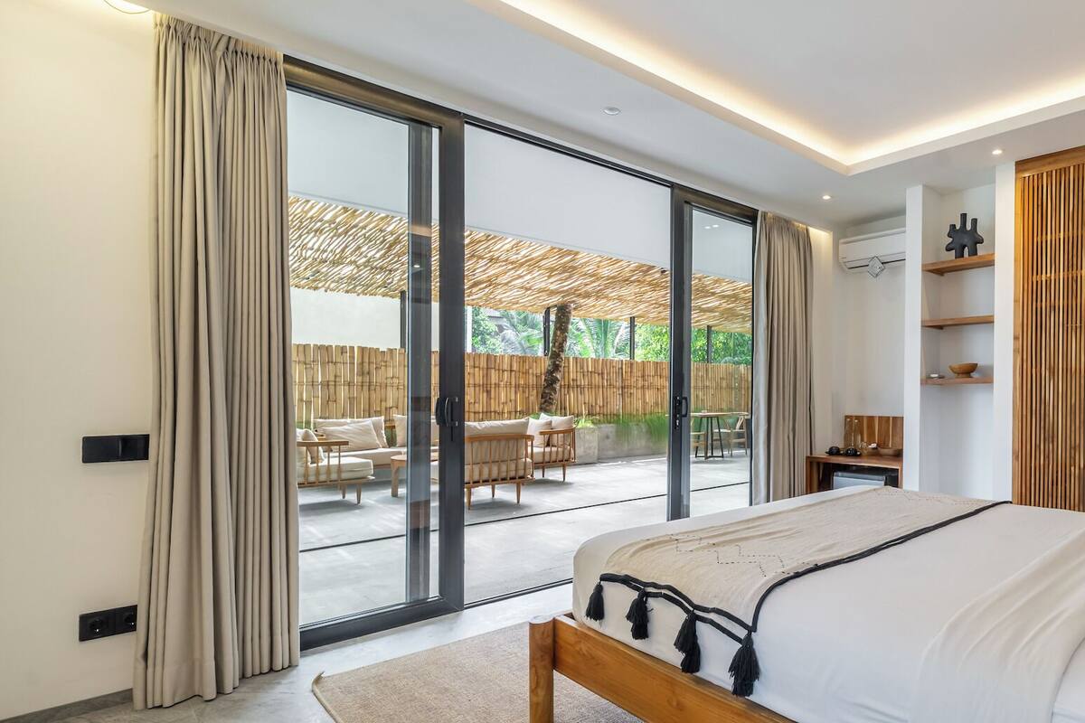 A modern bedroom with a large bed, sliding glass doors to an outdoor patio, and a minimalist design.